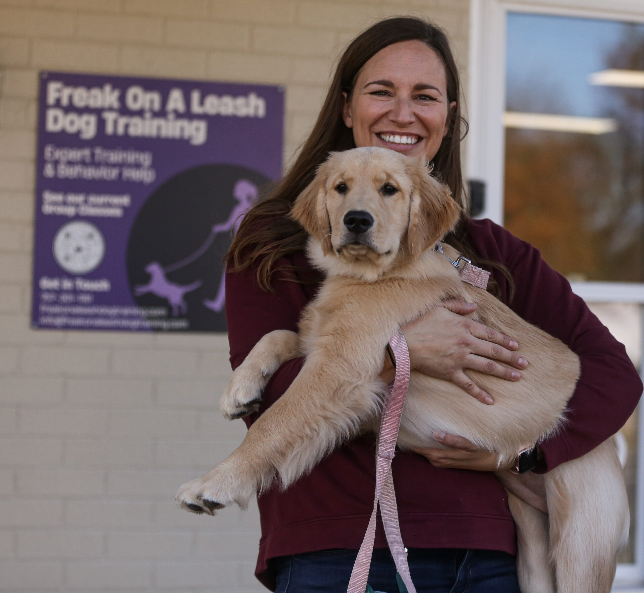 Golden Retriever puppy in the arms of smiling female owner in front of our facility in Chesapeake